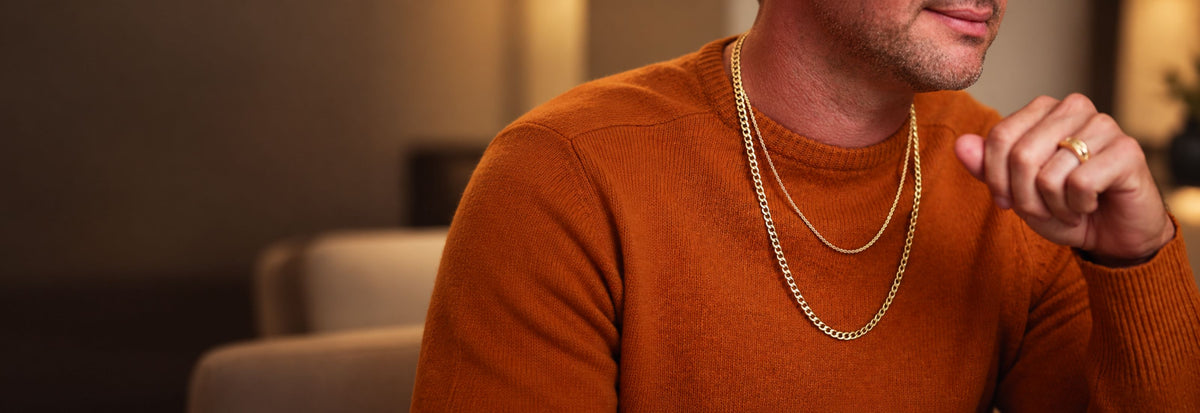 Man in an orange sweater wearing layered gold chains and a gold ring