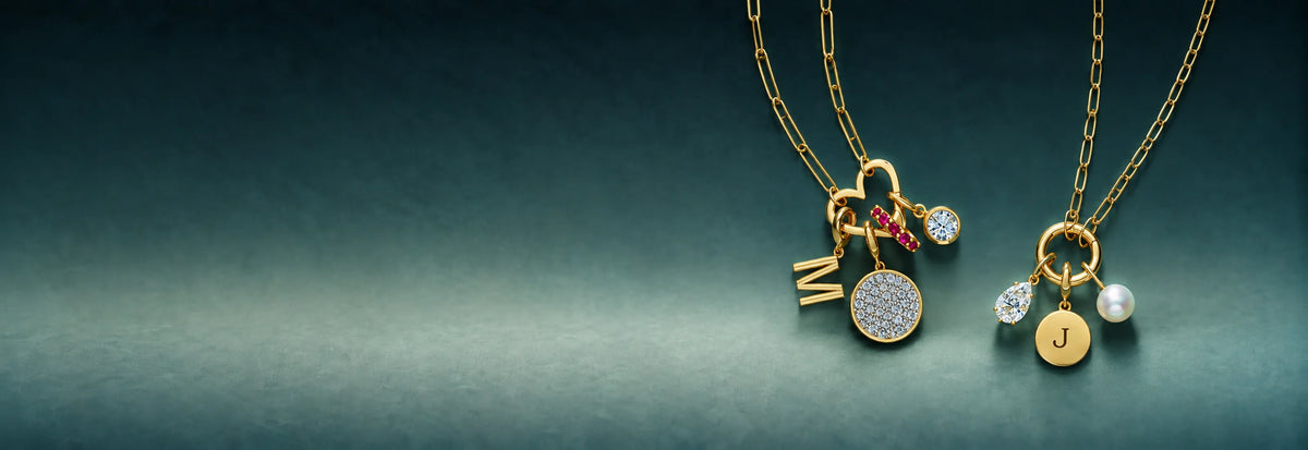 Gold charm necklaces with initial, heart and stone charms on a dark teal background