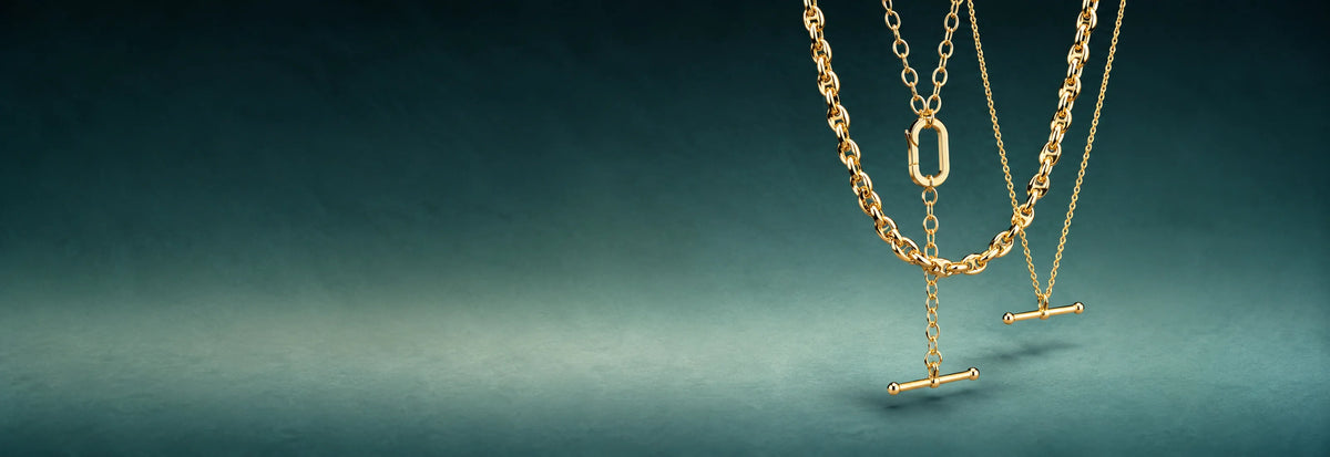 Layered yellow gold toggle and link necklaces on a teal background