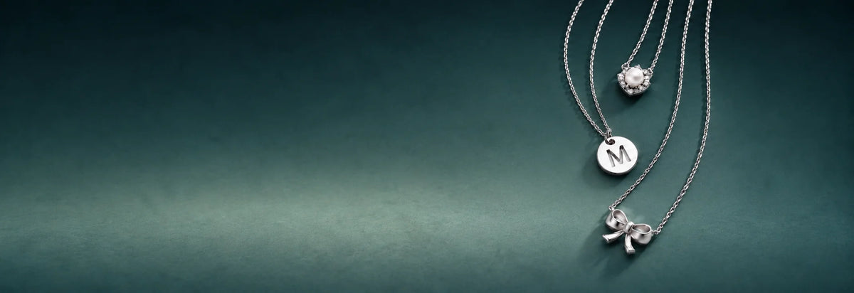 White gold initial and solitaire pendant necklaces on a dark teal background
