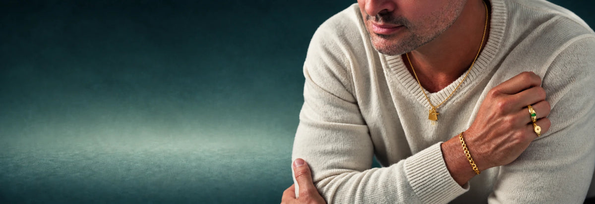 Man in a cream sweater wearing a gold chain, bracelet and ring