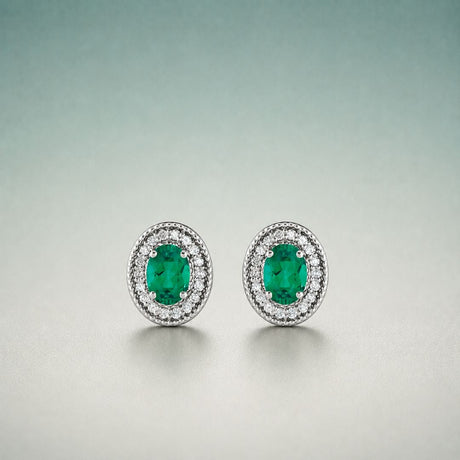 A pair of oval emerald stud earrings framed by small accent stones in a white metal setting