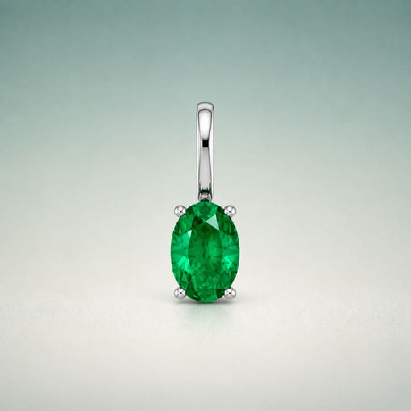 An oval emerald pendant held in a four-prong white metal setting with a long bail