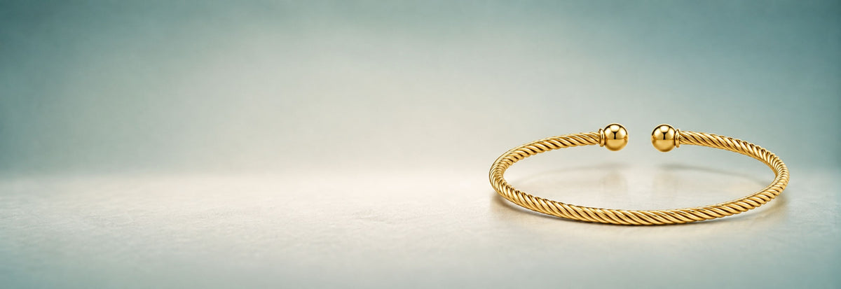 Yellow gold twisted cuff bangle on a soft teal background