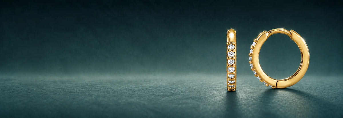 Yellow gold huggie hoop earrings with stones on a dark teal background
